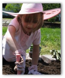 young girl digging in a garden with a hand trowel