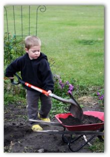 child shoveling dirt into a wheel barrow