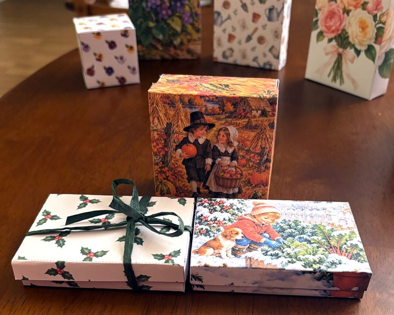 Holly and winter garden gift card boxes tied with green raffia, with a Pilgrim children box behind them