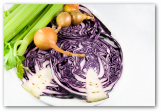 Halved purple cabbage arranged on a plate with celery and small onions